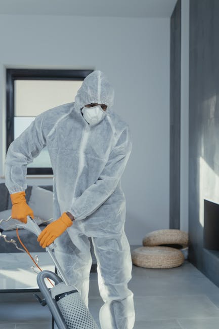 A close-up view of a home cleaning vacuum cleaner with a transparent dust container filled with dust and debris, connected to a flexible patterned hose and a black floor attachment. The vacuum is positioned on a pink carpeted floor inside a room with white walls and wooden skirting boards. The scene highlights surface cleaning equipment used for deep cleaning and hygiene maintenance, with the focus on the vacuum's components and the clean, well-maintained carpet surface. The company, Carpet Cleaning Highbury, specializes in domestic cleaning and surface sanitisation services, as seen in this professional cleaning setup.